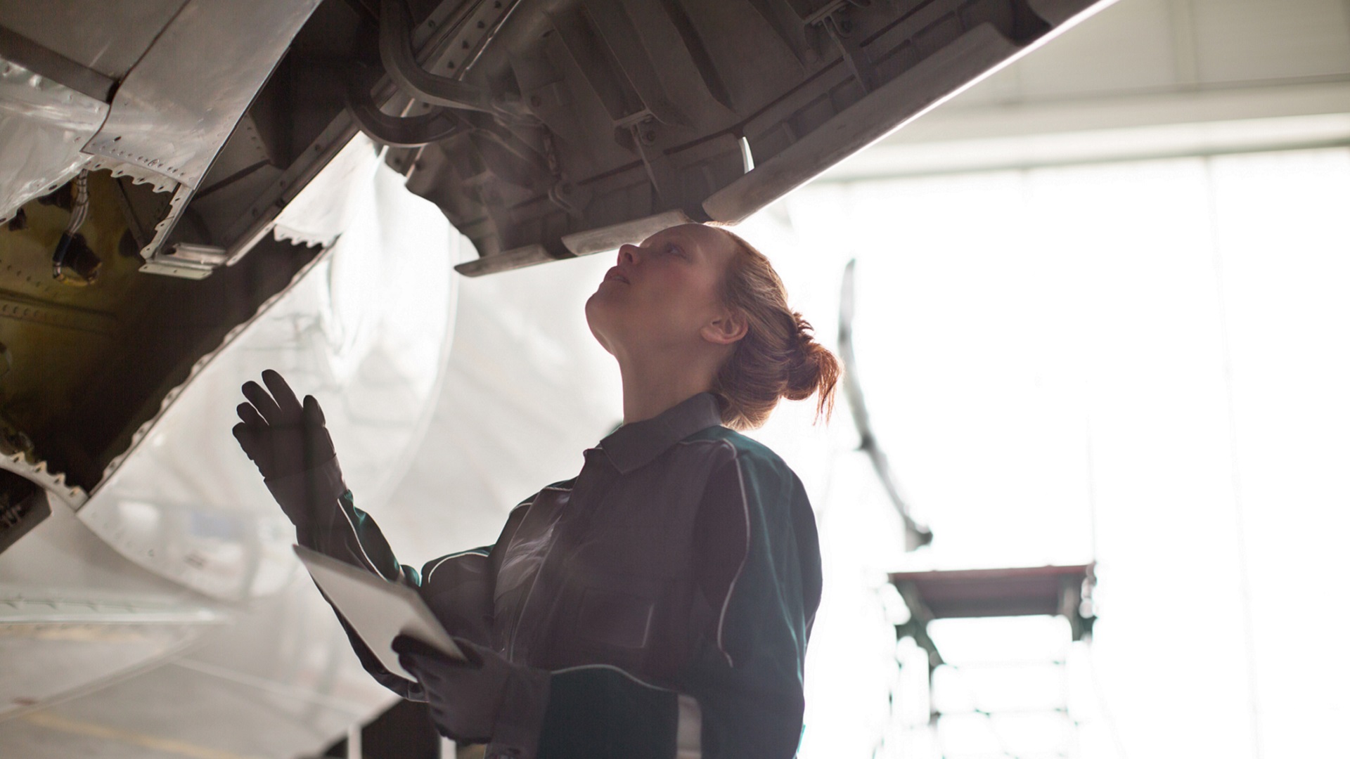 Female maintenance engineer inspecting airplane while holding digital PC in hangar