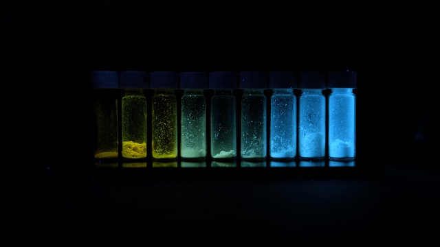 a line of the colour-changing polymer in beakers glowing yellow to green to blue.