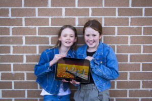 Two young girls in denim jackets holding a tablet showing the film they submitted and won a Eureka Prize.